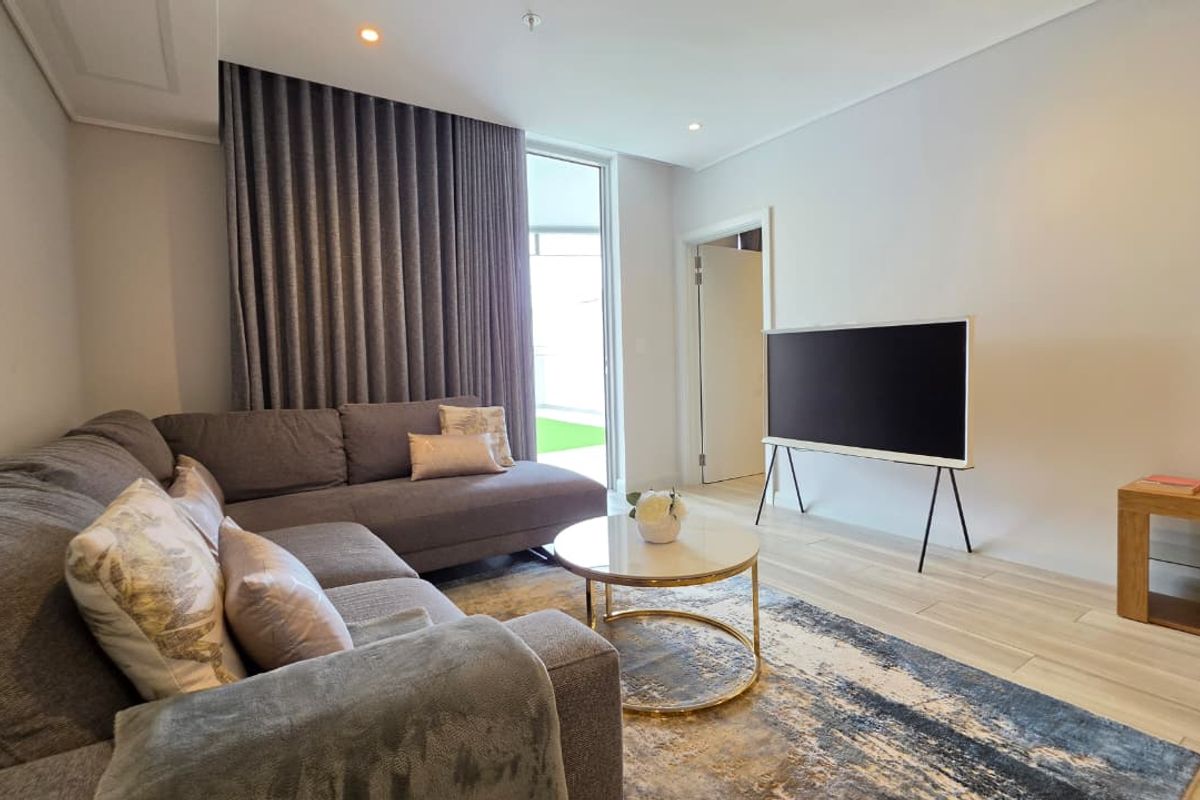 A bright and modern living room featuring wood-look tile flooring, recessed lighting, and a large sliding glass door providing access to the outdoor area.
