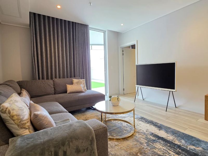 A bright and modern living room featuring wood-look tile flooring, recessed lighting, and a large sliding glass door providing access to the outdoor area.