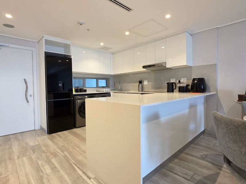 Modern open-plan kitchen featuring sleek white cabinetry, stone countertops, and integrated appliances, seamlessly flowing into the living and dining area.