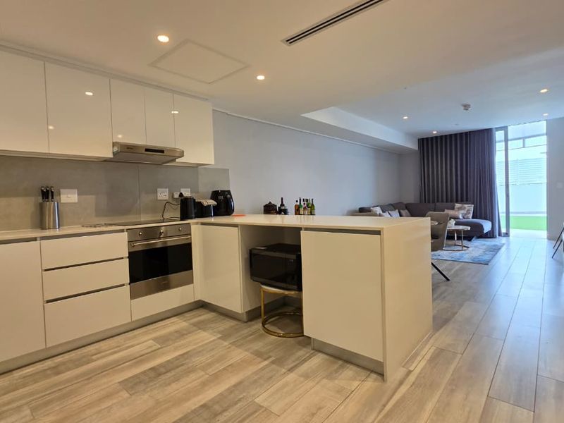 Modern open-plan kitchen and living area featuring sleek white cabinetry, integrated appliances, recessed lighting, and direct access to an outdoor patio space.