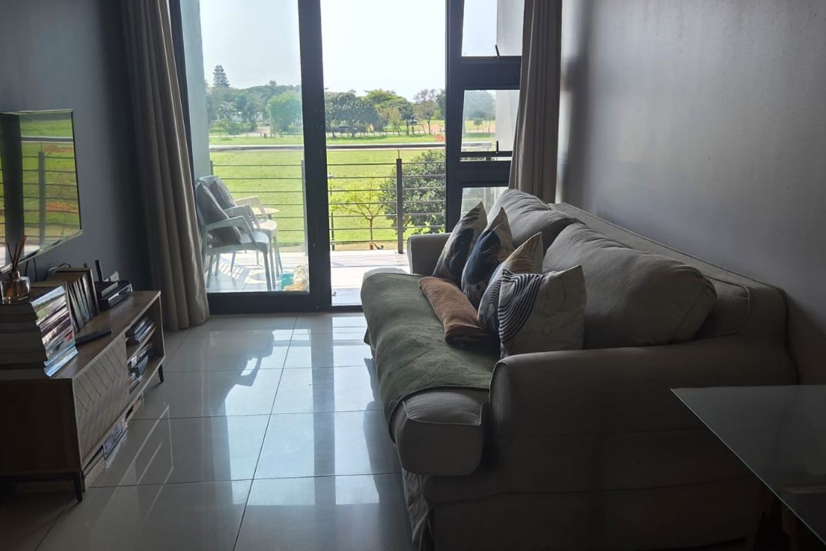 A well-lit living room featuring modern tiled flooring, decorative slat wall paneling, and large sliding glass doors that open onto a balcony with green views.