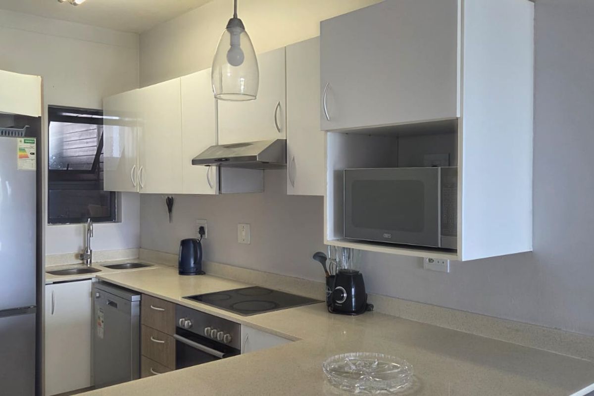 A functional kitchen featuring white cabinetry, stone countertops, integrated appliances, and a breakfast bar, with a modern pendant light fixture.