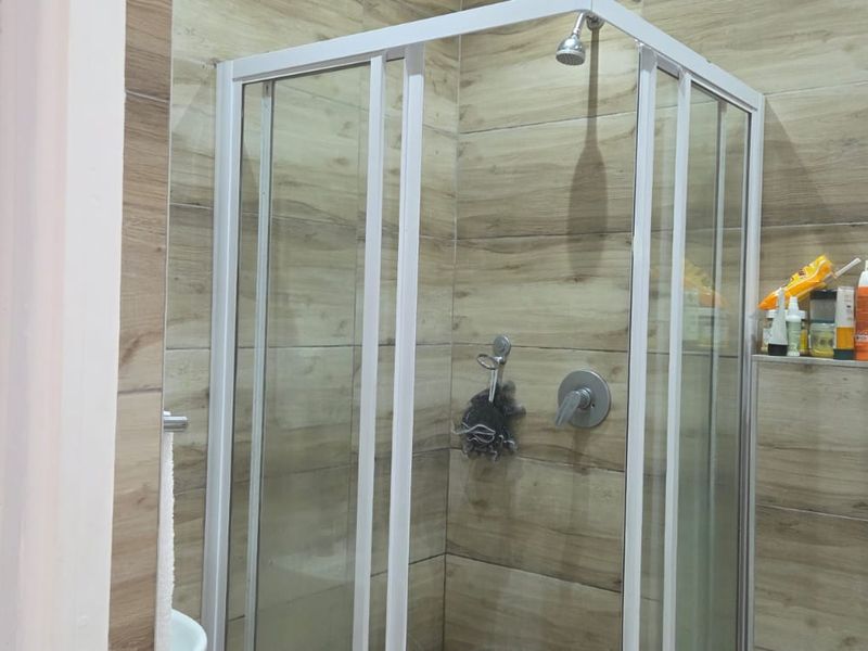 A modern bathroom featuring a glass-enclosed shower with wood-look wall tiling and a concealed cistern flush plate.