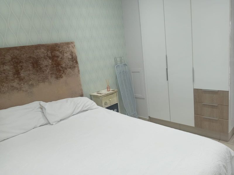 A well-maintained bedroom featuring built-in wardrobes with a combination of white and wood-grain finishes and decorative patterned wallpaper.