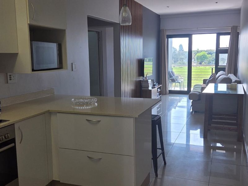 Modern open-plan kitchen and living area featuring sleek cabinetry, stone countertops, integrated appliances, and large sliding doors leading to a balcony.