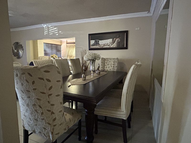 A dining room featuring tiled flooring and crown molding, with an open-plan layout leading into an adjacent living area.