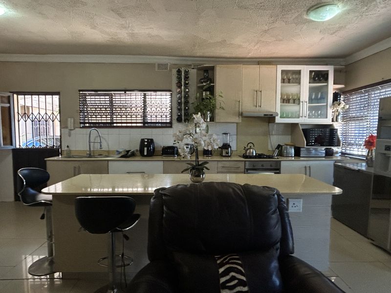 A functional kitchen featuring a central island, built-in cabinetry, gas hob, and tiled flooring, with a security gate leading to the exterior.