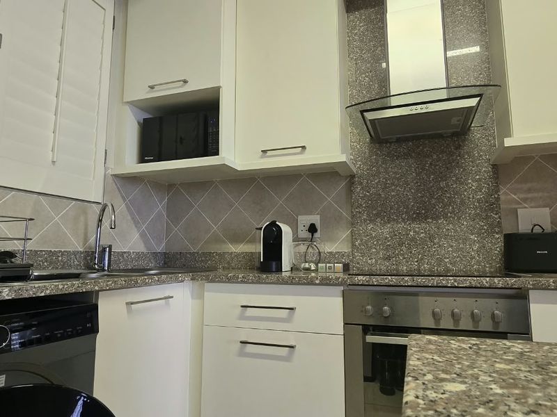 Modern kitchen featuring white cabinetry, granite countertops, tiled backsplash, and integrated stainless steel appliances including an oven and extractor fan.