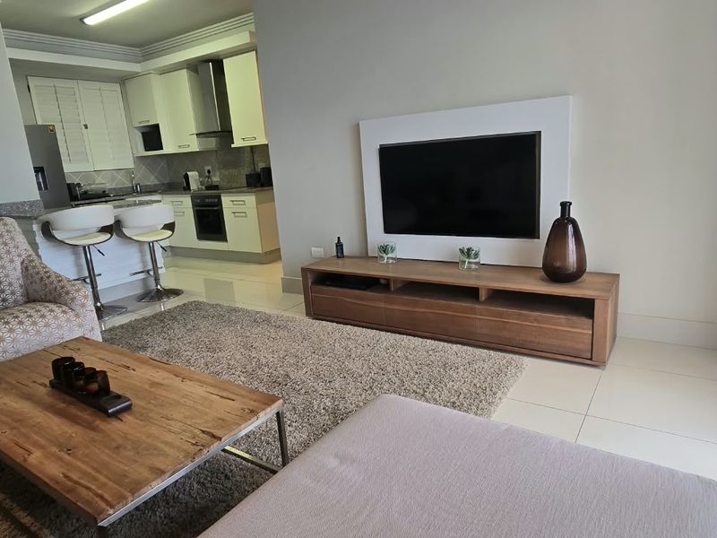 Open plan living area featuring a modern kitchen with built-in cabinetry, oven, and island, seamlessly flowing into a comfortable lounge space with tiled flooring.