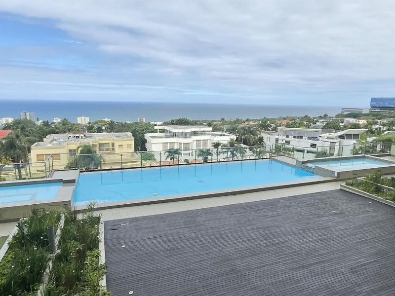 A well-maintained communal pool area featuring timber decking, glass balustrades, and expansive coastal views from the apartment complex.
