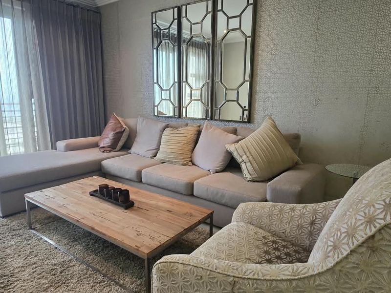 A well-maintained living room featuring patterned wallpaper, tiled flooring, and large sliding glass doors leading to a balcony.