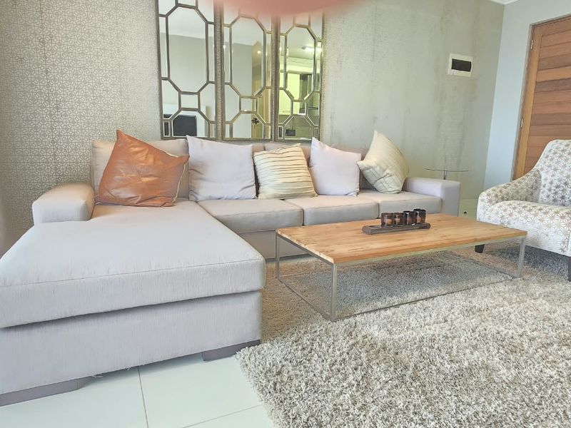 A well-maintained living room featuring tiled flooring, a solid timber door, and decorative wall mirrors, creating a bright and inviting space.