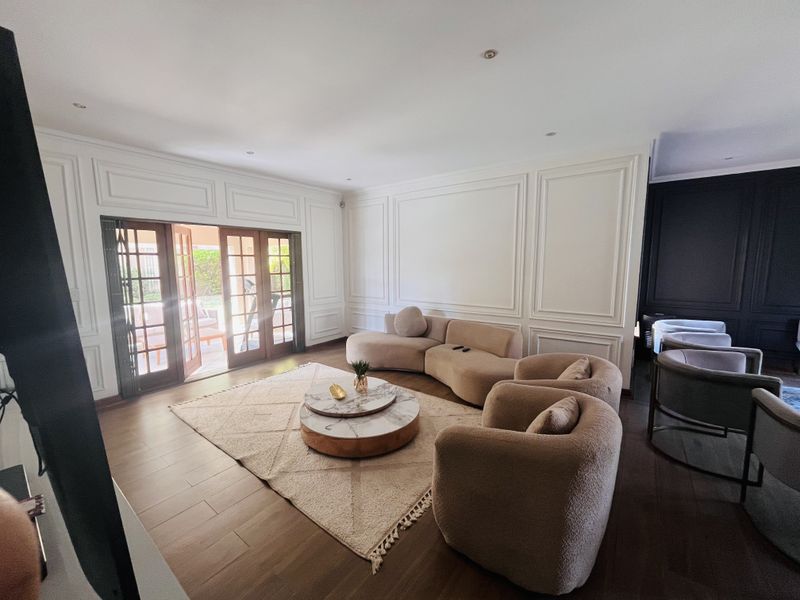 Elegant living room featuring sophisticated wainscoting, warm wooden flooring, recessed lighting, and large french doors providing seamless access to the outdoor area.