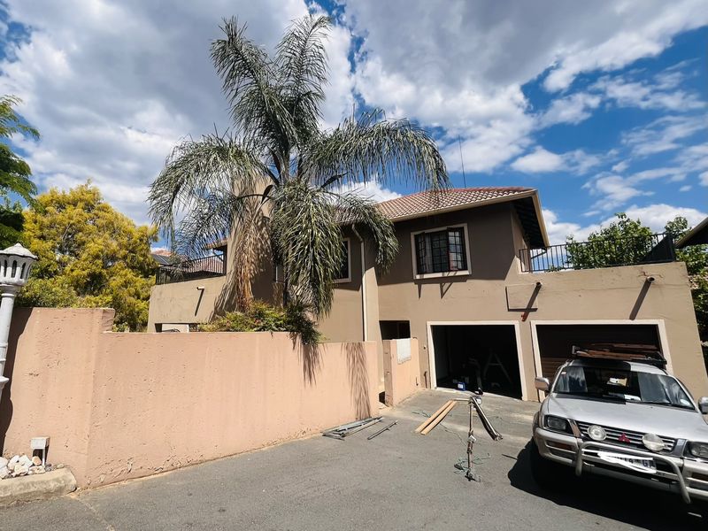 Front elevation of a double-story cluster home featuring a double garage, balcony with iron railings, and a perimeter boundary wall.