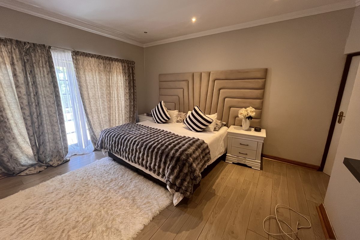 A well-maintained bedroom featuring laminate flooring, recessed downlighting, and a sliding glass door providing natural light and access to the exterior.