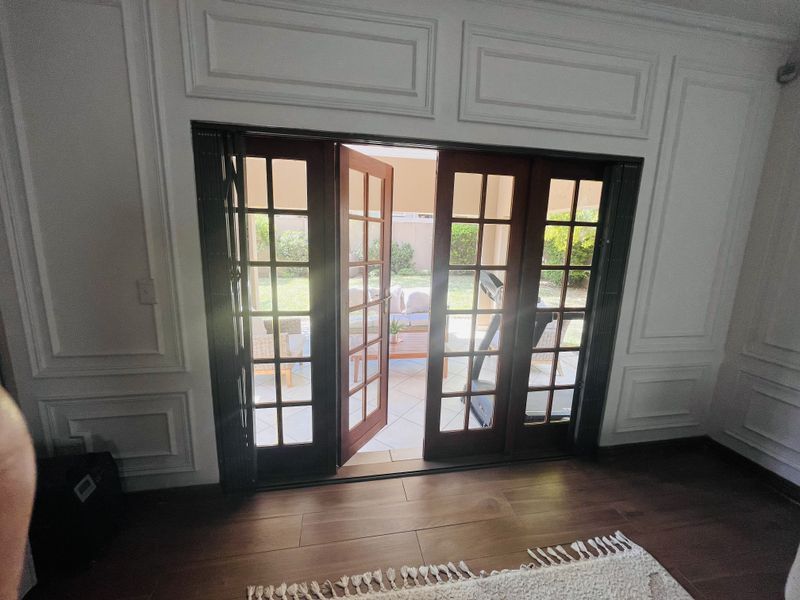 Spacious living area featuring elegant wainscoting, rich laminate flooring, and classic wooden French doors that open onto a private patio.