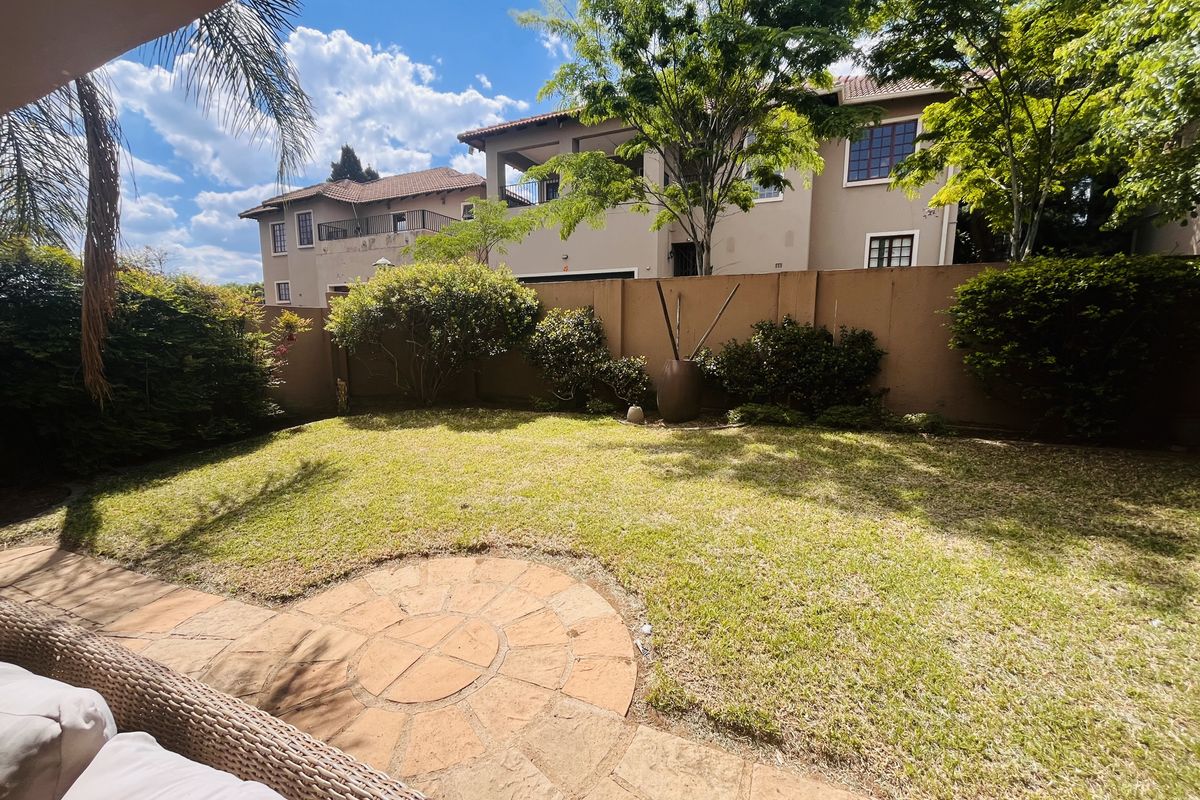 A private rear garden featuring a stone-paved patio area, a well-maintained lawn, and established boundary walls with mature landscaping.