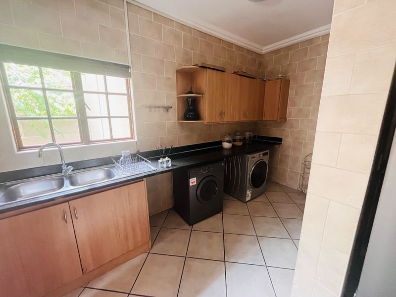 A functional laundry room featuring tiled walls and flooring, granite countertops, a double basin sink, and ample built-in wooden cabinetry.