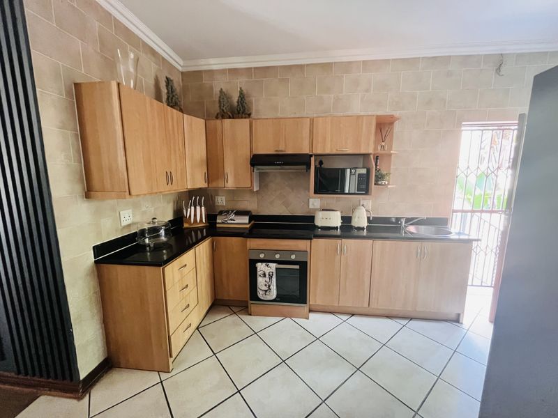 A functional kitchen featuring light wood cabinetry, black granite countertops, built-in oven, extractor fan, and tiled finishes throughout.