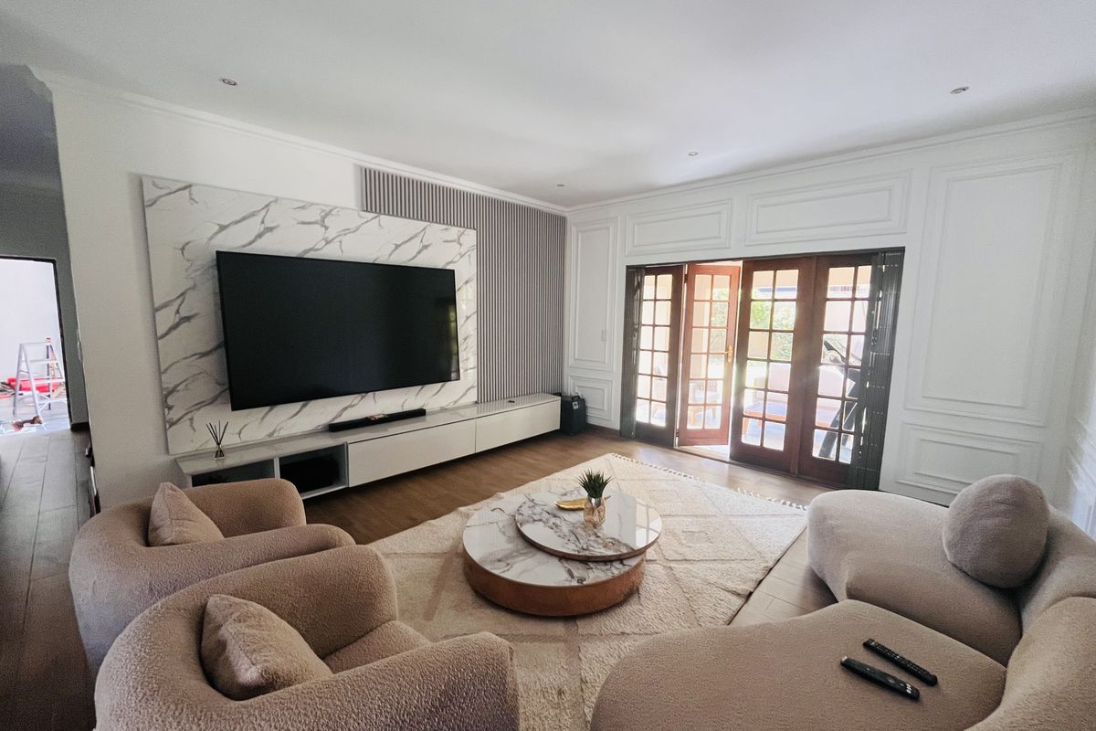 Spacious living room featuring a modern marble-look media wall, elegant wainscoting, and wooden French doors opening to the exterior.