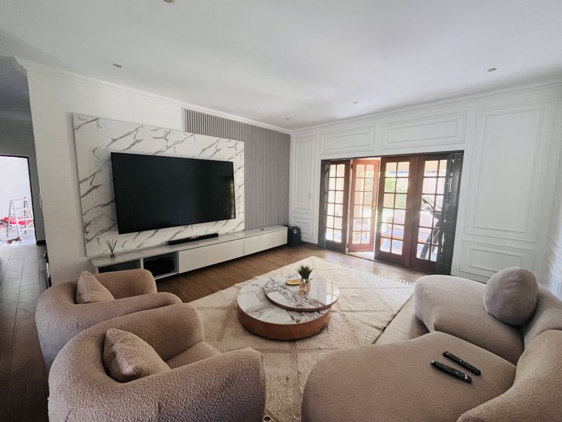 Spacious living room featuring a modern marble-look media wall, elegant wainscoting, and wooden French doors opening to the exterior.