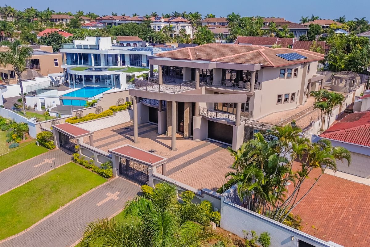 Aerial view of a large multi-story residential property featuring a paved driveway, double garage, balconies, and solar panels within a secure estate setting.