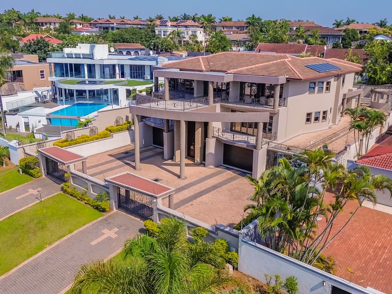 Aerial view of a large multi-story residential property featuring a paved driveway, double garage, balconies, and solar panels within a secure estate setting.