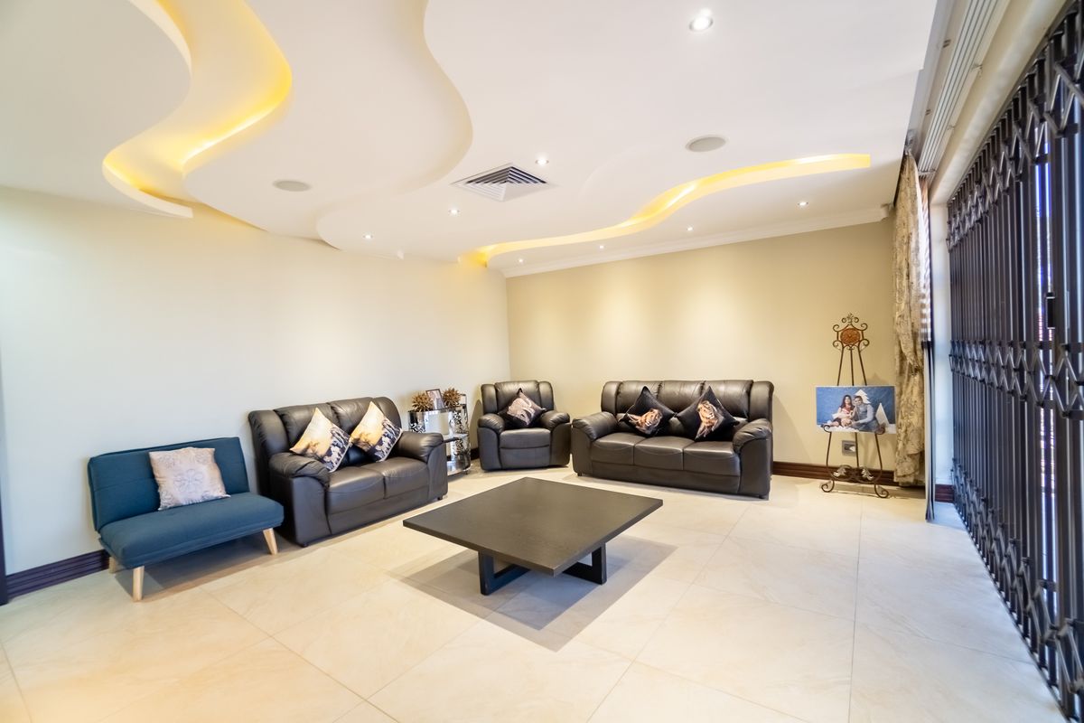 Spacious living room featuring a modern recessed ceiling with integrated cove lighting, ducted air conditioning, and neutral tiled flooring.