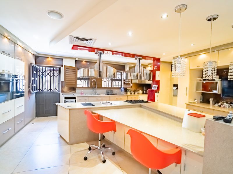 Modern kitchen featuring a large central island with stone countertops, integrated appliances, stainless steel extractor fans, and ample cabinetry with recessed lighting.