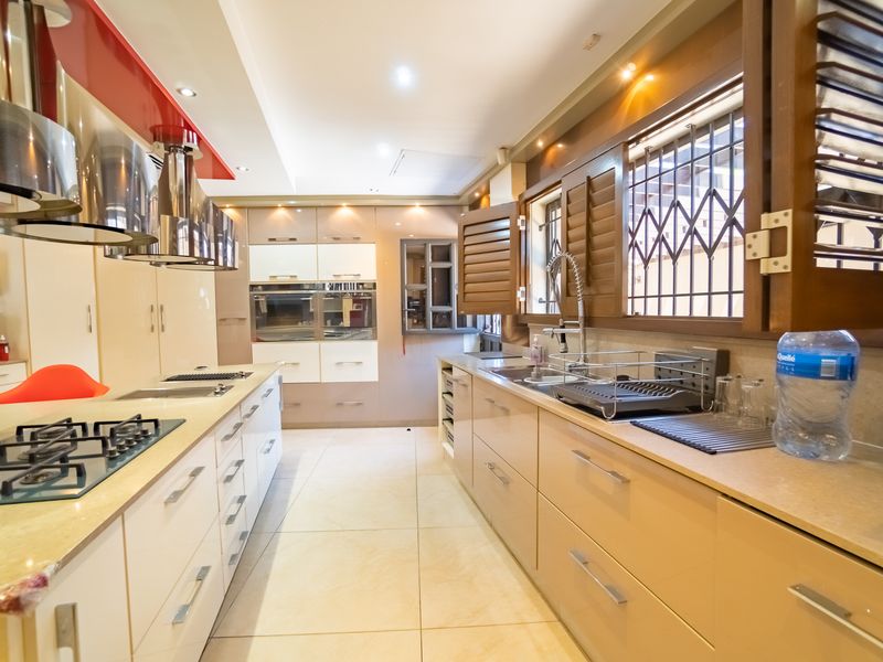 Modern kitchen featuring high-gloss cabinetry, integrated gas hob, stainless steel extractor fans, built-in oven, and tiled flooring with ample counter space.