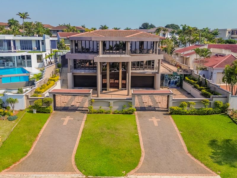 Aerial view of a large multi-story residential property featuring a paved driveway, double garage, and expansive balcony areas.