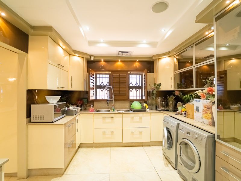 A well-appointed kitchen featuring high-gloss cabinetry, tiled flooring, recessed lighting, and integrated laundry appliances, offering a functional and modern workspace.