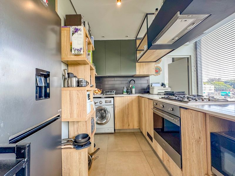 Modern kitchen featuring wood-finish cabinetry, stone countertops, integrated appliances including a gas hob, oven, and washing machine, complemented by a stylish subway tile backsplash.