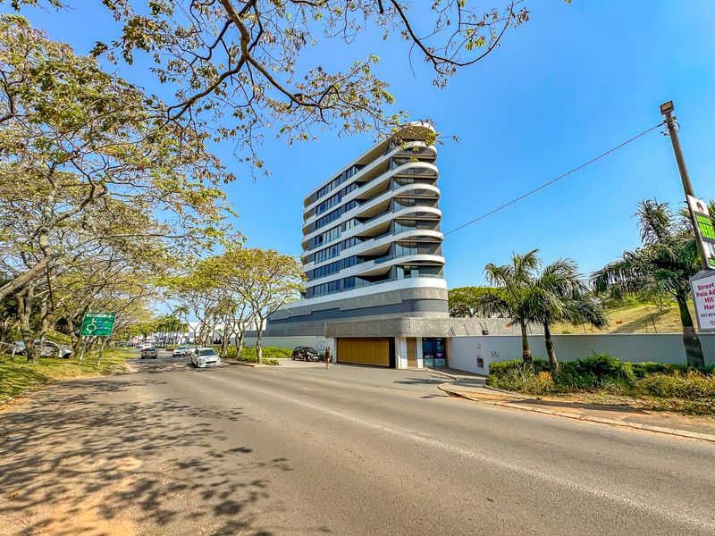 Street view of a modern, multi-story apartment building featuring distinctive curved balconies and a secure gated entrance.