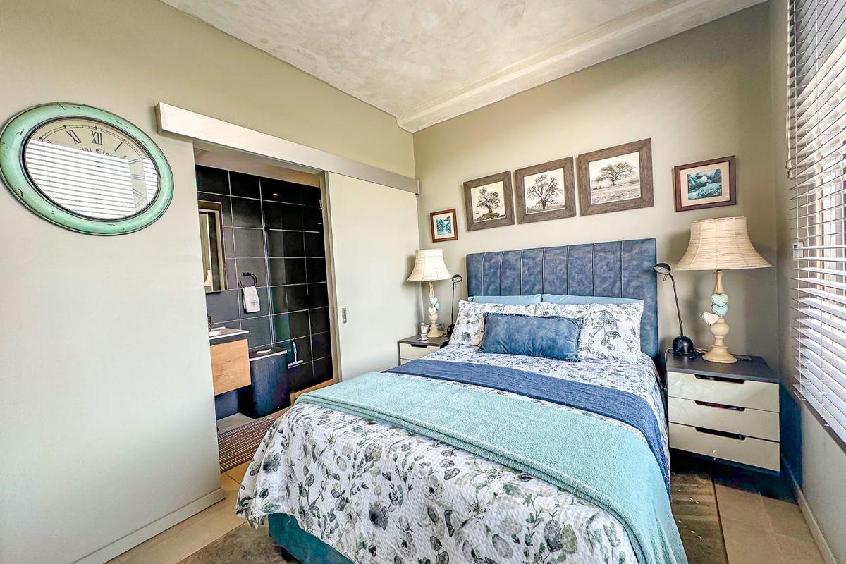 A well-maintained bedroom featuring an en-suite bathroom with a sliding door, neutral wall finishes, and venetian blinds.
