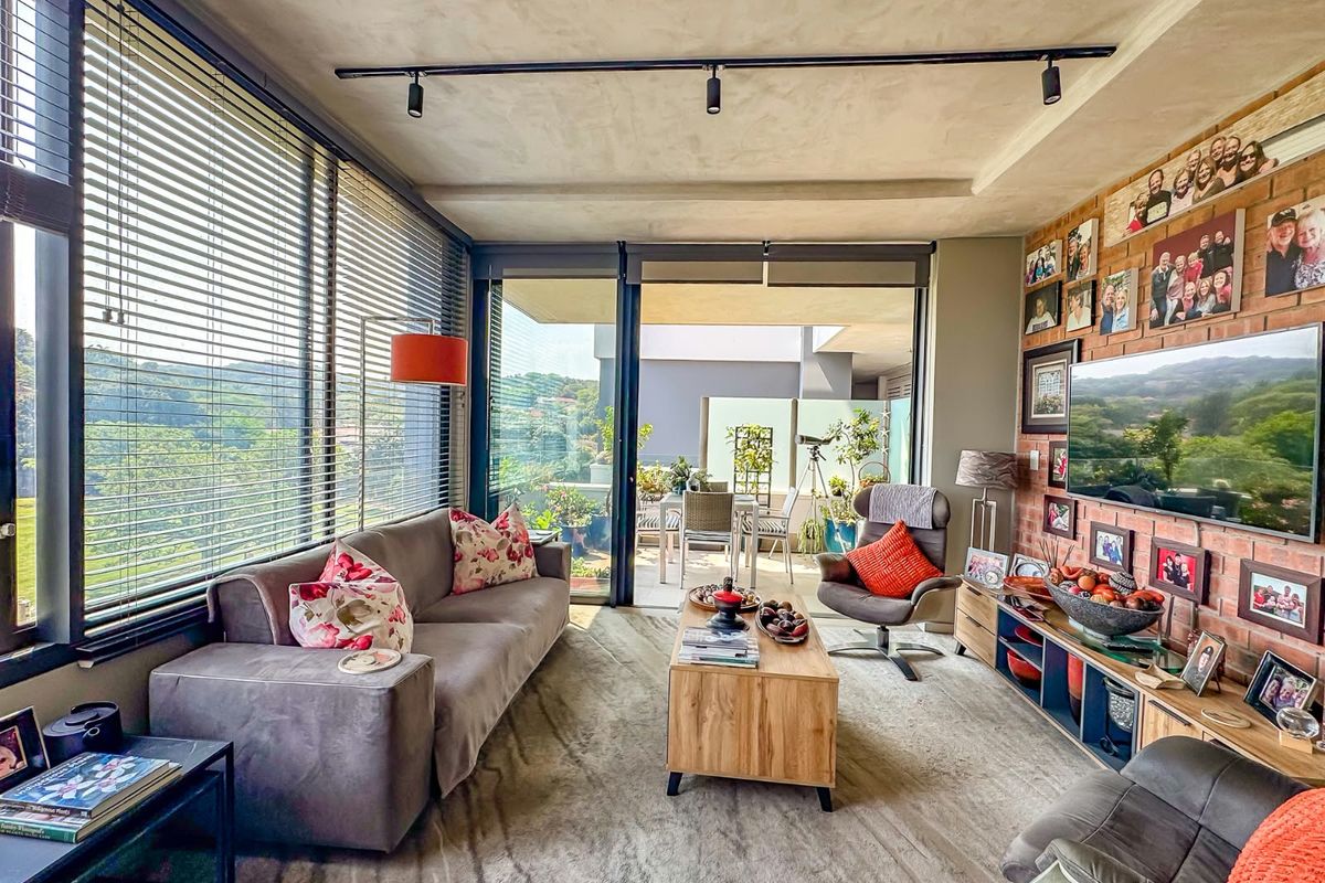 A bright living room featuring an exposed brick wall, track lighting, and large windows with access to a private balcony.