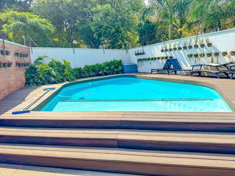 A well-maintained outdoor pool area featuring timber decking, a clear swimming pool, and perimeter walls with integrated vertical planters.