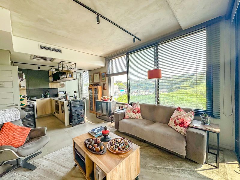 Modern open-plan living area featuring a sleek kitchen with built-in appliances, track lighting, and large windows with venetian blinds offering natural light.