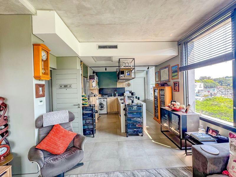 Modern open-plan apartment featuring a functional kitchen with integrated appliances, tiled flooring, and large windows providing ample natural light and scenic views.