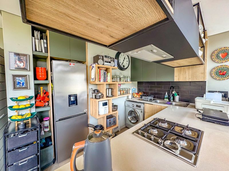 Modern kitchen featuring stone countertops, a gas hob, integrated washing machine, and stylish olive green and wood-tone cabinetry with a tiled backsplash.