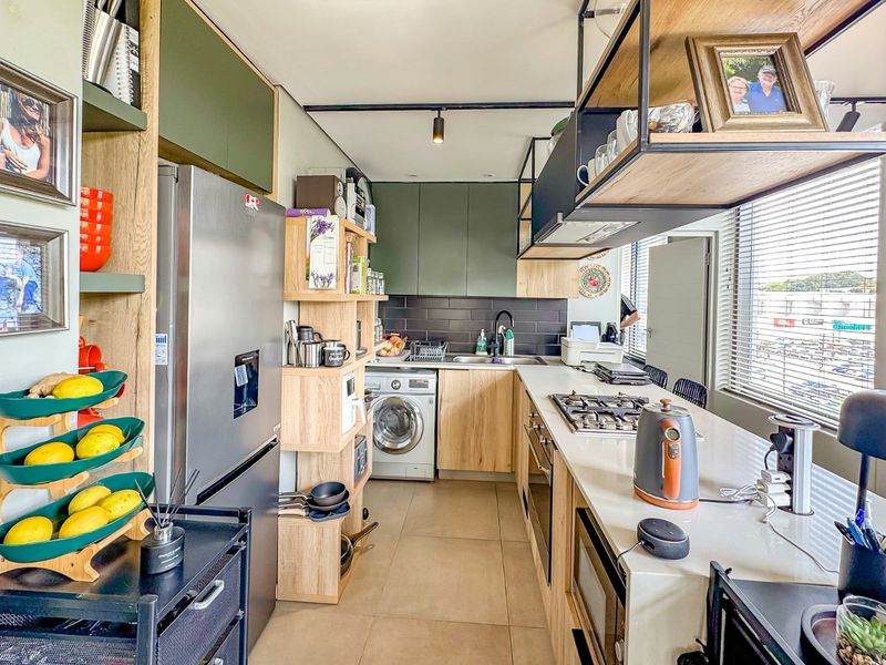 Modern kitchen featuring sleek green and wood-tone cabinetry, stone countertops, integrated appliances, and a functional layout with a gas hob and overhead shelving.