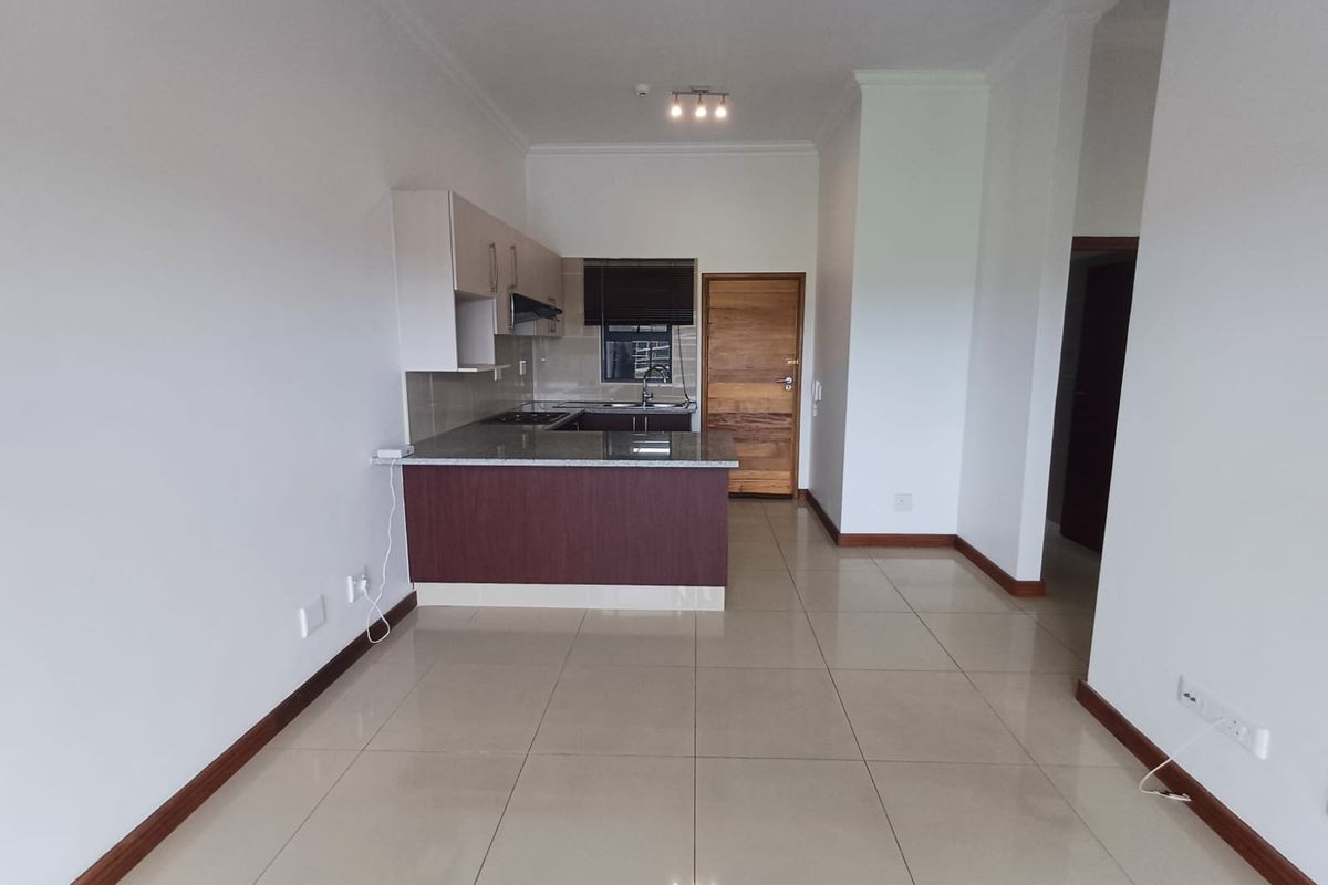 An open-plan living and kitchen area featuring tiled flooring, modern cabinetry with granite countertops, and a built-in hob, presenting a clean and well-maintained space.