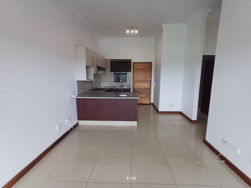 An open-plan living and kitchen area featuring tiled flooring, modern cabinetry with granite countertops, and a built-in hob, presenting a clean and well-maintained space.
