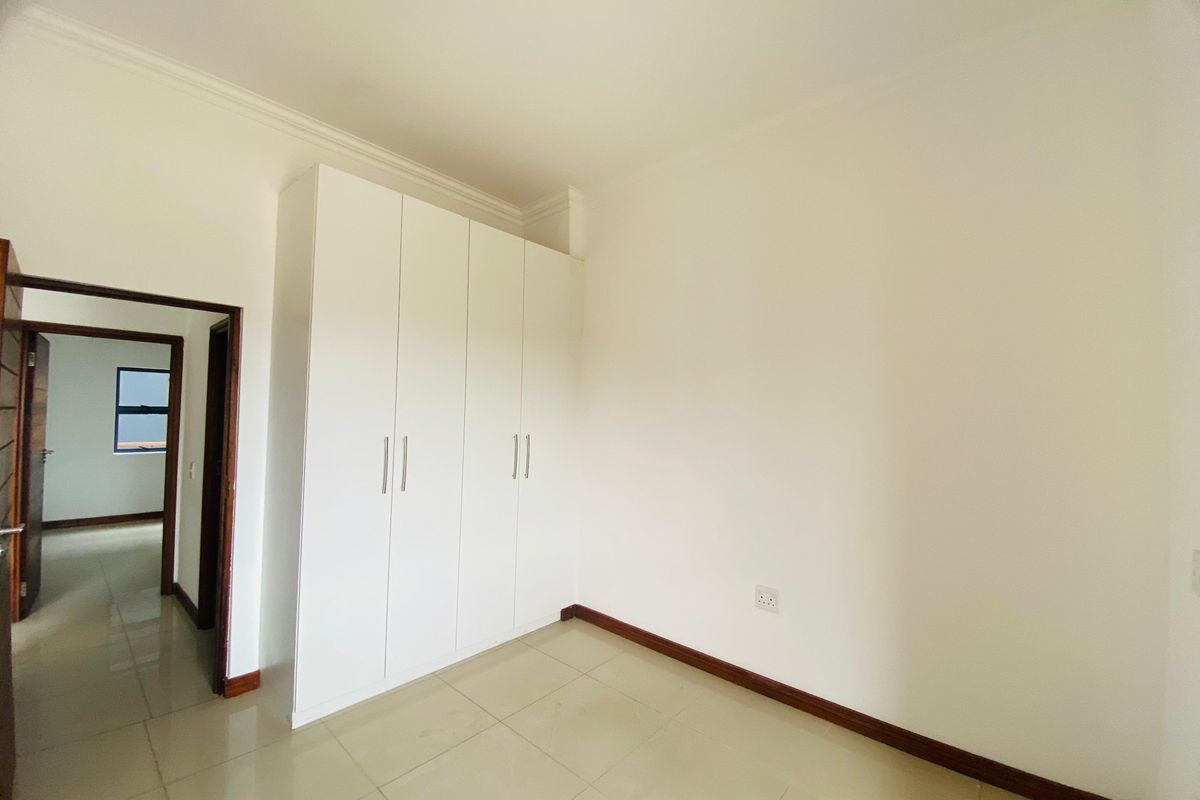 A clean, empty bedroom featuring neutral tiled flooring, white walls, and ample built-in cupboard storage space.