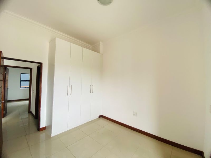 A clean, empty bedroom featuring neutral tiled flooring, white walls, and ample built-in cupboard storage space.
