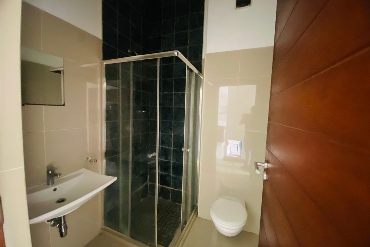 A modern bathroom featuring a wall-mounted basin, a glass shower enclosure with dark tiling, and a wall-hung toilet with a concealed cistern.