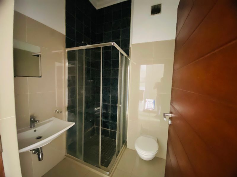 A modern bathroom featuring a wall-mounted basin, a glass shower enclosure with dark tiling, and a wall-hung toilet with a concealed cistern.