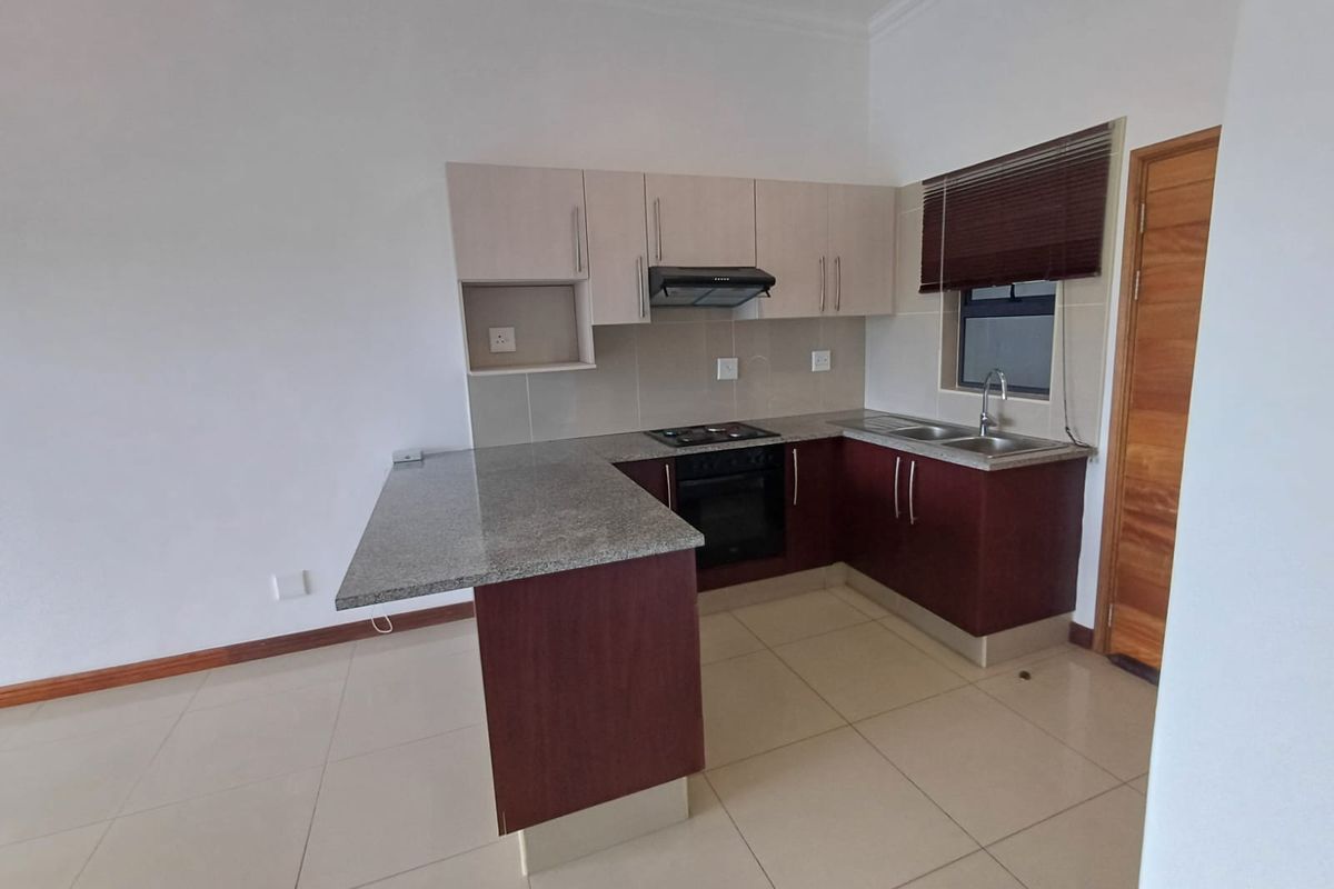 A clean, modern kitchen featuring granite countertops, built-in oven and hob, extractor fan, and ample cabinetry, finished with neutral tiled flooring.