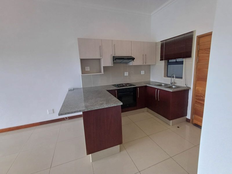 A clean, modern kitchen featuring granite countertops, built-in oven and hob, extractor fan, and ample cabinetry, finished with neutral tiled flooring.