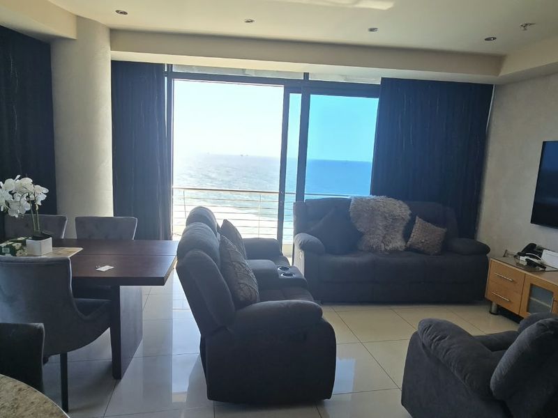 Spacious open-plan living and dining area featuring large sliding glass doors that open to a balcony with expansive ocean views.